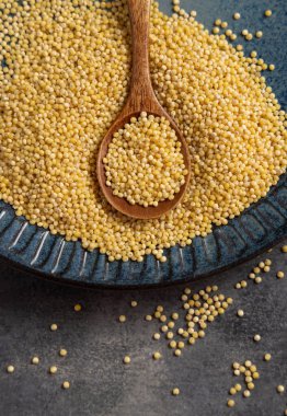 Mavi tabak çiğ sarı darı tahılı ve tahta kaşıkla gri masa manzaralı. Organik inci kabuklu darı. Eski, sağlıklı süper yiyecekler. Glütensiz alternatif tohumlar