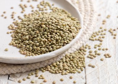 Tabak dolusu kurutulmuş çiğ yeşil mercimek beyaz masaya yakın. Sağlıklı çiğ vejetaryen yiyecekler, baklagiller bitkisel protein kaynakları. Geleneksel Akdeniz kuzen malzemesi