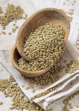 Ahşap kaseler keten peçetenin üstünde kurumuş yeşil mercimeklerle dolu. Sağlıklı vejetaryen yiyecekler, bitkisel protein kaynakları. Geleneksel Akdeniz çiğ kuzen malzemesi