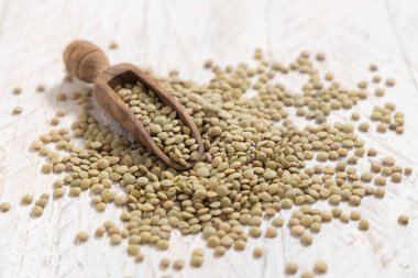 Beyaz masadaki kurutulmuş yeşil mercimek kepçesiyle dolu tahta kepçe. Sağlıklı vejetaryen yiyecekler, bitkisel protein kaynakları. Geleneksel Akdeniz çiğ kuzen malzemesi