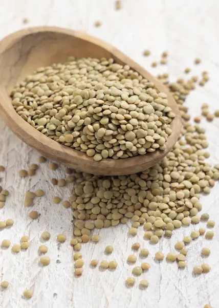 Tahta kase, beyaz masa üzerinde kurutulmuş yeşil mercimek. Sağlıklı çiğ vejetaryen yiyecekler, baklagiller bitkisel protein kaynakları. Geleneksel Akdeniz pişmemiş kuzen malzemesi