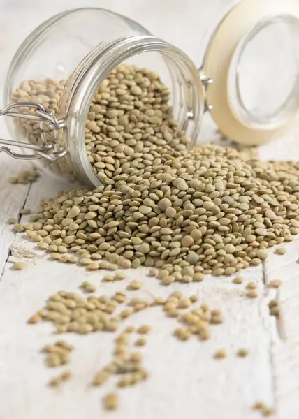 Beyaz masada içi kurutulmuş yeşil mercimek dolu cam kavanoz. Sağlıklı vejetaryen yiyecekler, bitkisel protein kaynakları. Geleneksel Akdeniz çiğ kuzen malzemesi