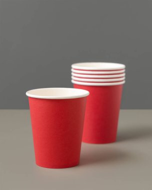 Koyu gri arka planda tek kullanımlık kırmızı bardaklar. Reklam alanı olan bir model. Boş karton kahve fincanları düz yerde. Plastik ve sürdürülebilir yaşam tarzı kavramı yok 
