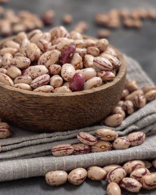 Gri masadaki peçetenin üzerinde kurumuş fasulye dolu ahşap kase. Sağlıklı vejetaryen yemekleri, protein kaynakları. Geleneksel Latin Amerikalı kuzen malzemesi