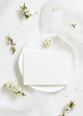 Tulle 'ün yanındaki tabakta boş kart ve yaban erikleri üst manzaralı beyaz çiçekler, maket. Doğaya yakın bahar partisi tasarımı için Pastel yatay kart, anneler günü veya romantik düğün kırtasiyesi