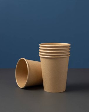 Tek kullanımlık bej kağıt bardaklar koyu griye karşı mavi yakın plan, reklam alanı olan bir model. Boş karton kahve fincanları. Plastik ve sürdürülebilir yaşam tarzı kavramı yok 