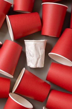 Tek kullanımlık kırmızı bardaklar ve buruşmuş beyaz bardaklar. Boş tek kullanımlık karton kahve fincanları düz yerde. Modern dünyada tüketim kavramı