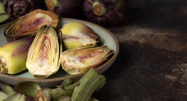 Koyu kırsal masa üzerinde kesilmiş mor, ham romanesko enginarlarla dolu bir tabak. Yakın plan, kopyalama alanı. Çiftçi pazarından alınmış taze sebzeler. Temizlik yapıyor ve yemek yapmaya hazırlanıyor. İtalyan kuzeni.