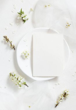 Tulle 'ün yanındaki tabakta boş kart ve yaban erikleri üst manzaralı beyaz çiçekler, maket. Doğaya yakın bahar partisi tasarımı için Pastel dikey kart, anneler günü veya romantik düğün kırtasiyesi
