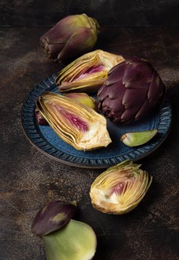 Koyu kırsal masa üzerinde mor, çiğ romanesko enginarlarla dolu mavi bir tabak. Çiftçi pazarından alınmış taze sebzeler pişirmeye hazır. İtalyan kuzeni.