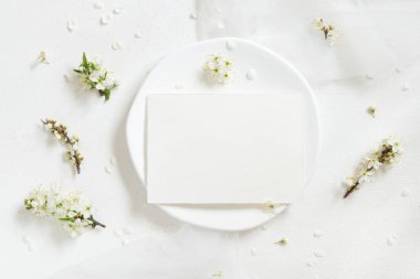 Tulle 'ün yanındaki tabakta boş kart ve yaban erikleri üst manzaralı beyaz çiçekler, maket. Doğaya yakın bahar partisi tasarımı için Pastel yatay kart, anneler günü veya romantik düğün kırtasiyesi