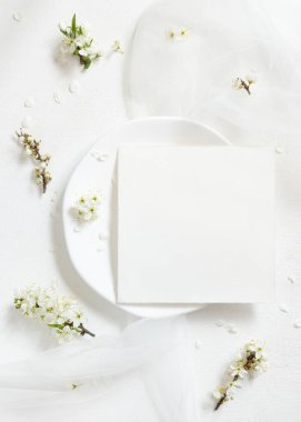 Tulle 'ün yanındaki tabakta boş kart ve yaban erikleri üst manzaralı beyaz çiçekler, maket. Pastel kare kart doğaya yakın bahar partisi tasarımı, anneler günü veya romantik düğün kırtasiyesi için.