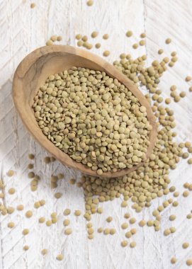 Tahta kase beyaz masa manzaralı kurutulmuş yeşil mercimeklerle dolu. Sağlıklı çiğ vejetaryen yiyecekler, baklagiller bitkisel protein kaynakları. Geleneksel Akdeniz pişmemiş kuzen malzemesi