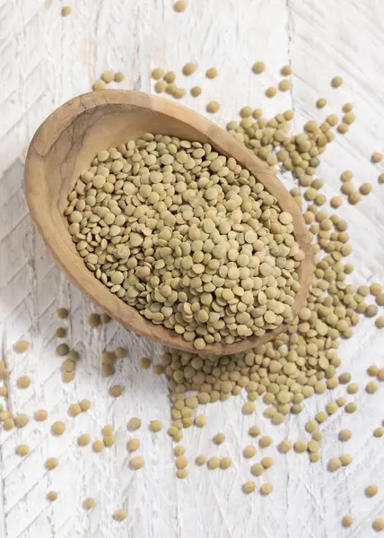 Tahta kase beyaz masa manzaralı kurutulmuş yeşil mercimeklerle dolu. Sağlıklı çiğ vejetaryen yiyecekler, baklagiller bitkisel protein kaynakları. Geleneksel Akdeniz pişmemiş kuzen malzemesi