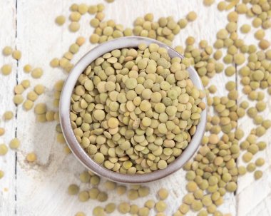 Beyaz masa manzaralı küçük bir kâse dolusu kuru yeşil mercimek. Sağlıklı vejetaryen yiyecekler, bitkisel protein kaynakları. Geleneksel Akdeniz çiğ kuzen malzemesi