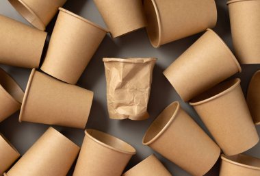 Tek kullanımlık yeni bej renkli kağıt bardaklar ve kırışmış gri üst görünümde bir tane. Boş karton, tek kullanımlık kahve fincanları düz yerde. Modern dünyada tüketim kavramı