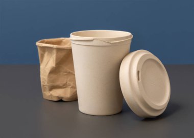 Kullanılmış ve buruşmuş kağıt bardak ve yeniden kullanılabilir bambu kahve bardağını gri üzerine mavi yakın plan, kopyalama alanı, maket. Tüketim konsepti. Plastik ve sürdürülebilir yaşam tarzı kavramı yok 