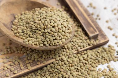 Tahta kase, beyaz masada kurutulmuş çiğ yeşil mercimek. Sağlıklı çiğ vejetaryen yiyecekler, baklagiller bitkisel protein kaynakları. Geleneksel Akdeniz malzemesi