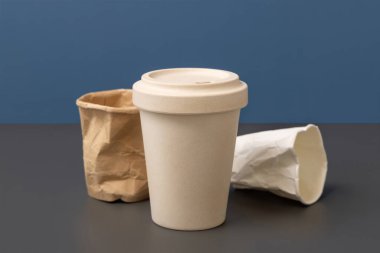 Kullanılmış ve buruşmuş kağıt bardaklar ve gri üzerine tekrar kullanılabilir bambu kahve fincanı mavi yakın plan, kopyalama alanı, maket. Tüketim konsepti. Plastik ve sürdürülebilir yaşam tarzı kavramı yok 
