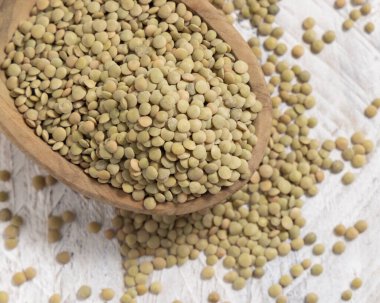 Tahta kase beyaz masa manzaralı kurutulmuş yeşil mercimeklerle dolu. Sağlıklı çiğ vejetaryen yiyecekler, baklagiller bitkisel protein kaynakları. Geleneksel Akdeniz pişmemiş kuzen malzemesi