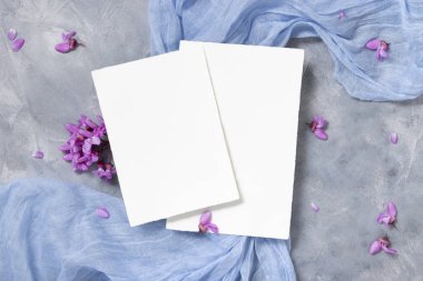 Mor çiçeklerin yanında açık mavi kumaş üzerindeki boş kartlar üst görünüm, pastel maketler. Bahar partisi tasarımı ya da romantik düğün kırtasiyesi için dikey kartlar. Doğaya yakın ya da anneler günü yatıyordu