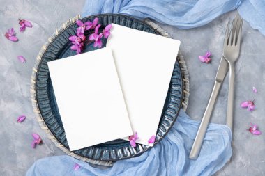 Pastel düğün masasında açık mavi kumaş ve mor çiçeklerle süslenmiş bir yer. Bahar partisi tasarımı ya da romantik düğün kırtasiyesi için dikey boş kartlar 