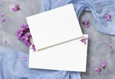 Mor çiçeklerin yanında açık mavi kumaş üzerindeki boş kartlar üst görünüm, pastel maketler. Bahar partisi tasarımı ya da romantik düğün kırtasiyesi için yatay kartlar. Doğaya yakın ya da anneler günü yatıyordu
