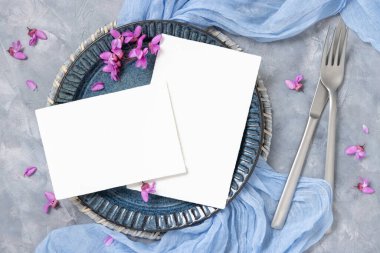 Pastel düğün masasında açık mavi kumaş ve mor çiçeklerle süslenmiş bir yer. Bahar partisi tasarımı ya da romantik düğün kırtasiyesi için boş kartlar. 