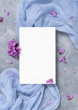 Mor çiçeklerin yanında açık mavi kumaş üzerindeki boş kartlar üst görünüm, pastel maketler. Bahar partisi tasarımı ya da romantik düğün kırtasiyesi için dikey kart. Doğaya yakın ya da anneler günü yatıyordu