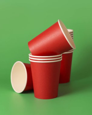 Yeşil arka planda tek kullanımlık kırmızı bardaklar. Reklam alanı olan bir model. Boş karton kahve fincanları. Plastik ve sürdürülebilir Noel kavramı yok 