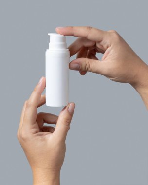 Beyaz kozmetik pompa şişesi tutan kadın eller Grey 'e karşı yakın çekim, paket modeli, kopyalama alanı. Cilt kremi - losyon ya da krem