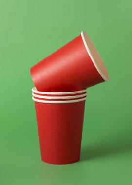 Yeşil arka planda tek kullanımlık kırmızı bardaklar. Reklam alanı olan bir model. Boş karton kahve fincanları. Plastik ve sürdürülebilir Noel kavramı yok 