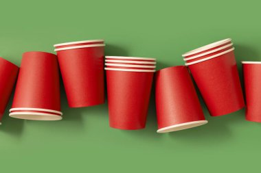 Yeşil arkaplan manzaralı tek kullanımlık kırmızı bardaklar, reklam alanı olan maketler. Boş karton kahve fincanları. Plastik ve sürdürülebilir Noel kavramı yok 
