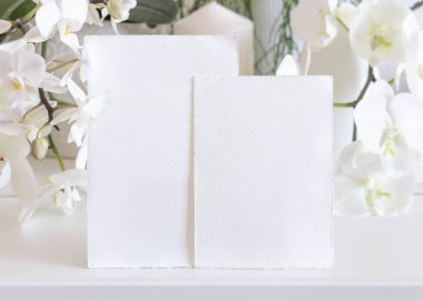 Masada beyaz orkide çiçeklerinin yanındaki boş kartlar yakın plan, maket. Egzotik düğün, sevgililer günü ya da anneler günü kırtasiyesi ve tropikal parti tasarımı için dikey kartlı Pastel romantik sahne