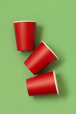 Yeşil arkaplan manzaralı tek kullanımlık kırmızı bardaklar, reklam alanı olan maketler. Boş karton kahve fincanları. Plastik ve sürdürülebilir Noel kavramı yok 
