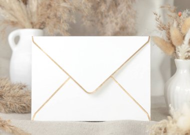 Bej pampalara karşı altın kenarlı zarf keten masa örtüsü üzerine çimen buketleri, maket. Boş zarflı boho sahnesi, bohem ya da doğaya yakın düğün kırtasiyesi