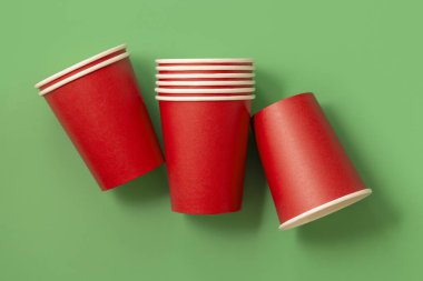 Yeşil arkaplan manzaralı tek kullanımlık kırmızı bardaklar, reklam alanı olan maketler. Boş karton kahve fincanları. Plastik ve sürdürülebilir Noel kavramı yok 