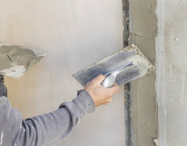 Zanaatkar, evin duvarını kaplamak için şamandıra ve çimento kullanıyor. İnşaat veya yenileme çalışmaları sırasında gri iş elbiseli genç erkekler