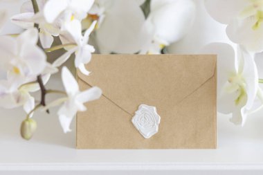 Beyaz orkide çiçeklerinin yanındaki mühürlü zarf. Masaya yakın, maket. Egzotik düğün, Sevgililer Günü ya da Anneler Günü kırtasiyesi ve tropikal parti tasarımı için yatay kartlı Pastel romantik sahne