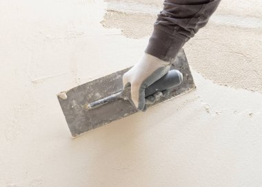 Zanaatkar, evin duvarını kaplamak için şamandıra ve çimento kullanıyor. İnşaat veya yenileme çalışmaları sırasında gri iş elbiseli genç erkekler
