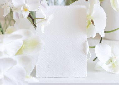 Beyaz orkide çiçeklerinin yanındaki boş kart. Masaya yakın, maket. Egzotik düğün, Sevgililer Günü ya da Anneler Günü kırtasiyesi ve tropikal parti tasarımı için dikey kartlı Pastel romantik sahne