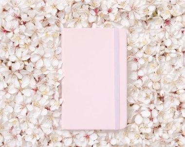 Beyaz kiraz çiçeklerinin üzerine açık pembe bir defter beyaz masa, kopyalama alanı, maket. Okul ya da mandıra için Spiral ciltli ders kitabı, bahar havası