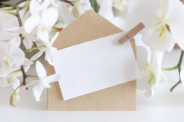 Kart ve zarf beyaz orkide çiçeklerinin yanında. Masanın üstünde, yakın plan, maket. Egzotik düğün, Sevgililer Günü ya da Anneler Günü kırtasiyesi ve tropikal parti tasarımı için yatay kartlı Pastel romantik sahne