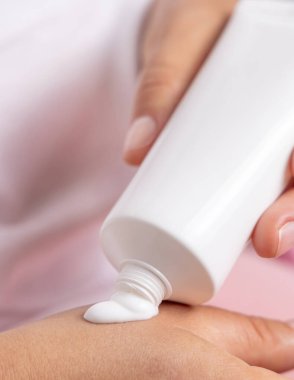 Beyaz tişörtlü, el kremi sıkan ve diğer elinde tüp tutan bir kadın. Güzellik ya da güzellik salonunda el bakımı, doğal kozmetik modelleme.
