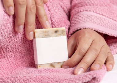Doğal manikürlü kadın elleri boş etiketli sabun kalıbı, ambalaj modeli. Banyoda açık pembe bornoz giyen bir kadın. Hijyen kavramı