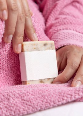 Doğal manikürlü kadın elleri boş etiketli sabun kalıbı, ambalaj modeli. Banyoda açık pembe bornoz giyen bir kadın. Hijyen kavramı