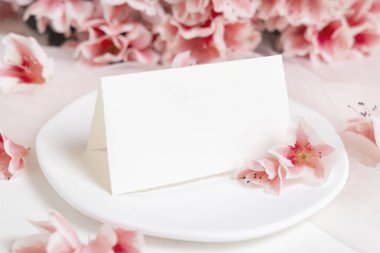 Pembe açelya çiçeklerinin yanındaki tabakta katlanmış kağıt kart yakın plan, kopyalama alanı, maket. Bahar romantik düğün kırtasiyesi ya da parti tasarımı için yatay kart, Anneler Günü ya da doğum günü havası