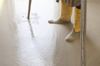 Sarı lastik çizme giyen bir adam yeni binadaki ısıtma tesisatının üzerine sıvı beton döküyor. Yeni ev inşaatında modern ısıtma sistemi