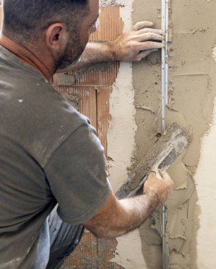 Zanaatkar, evin duvarını kaplamak için şamandıra ve çimento kullanıyor. İnşaat ve yenileme çalışmaları sırasında eldivenli ve gri elbiseli adamlar