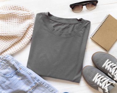 Kot pantolonlar, güneş gözlükleri, atkı ve spor ayakkabıları arasında beyaz tahta tahta üst manzarada boş, katlanmış kömür grisi tişört, maket. Üniseks kıyafetleri düz şablon şeklinde. Aksesuarlarla yaz tatili. Gömlek izi 